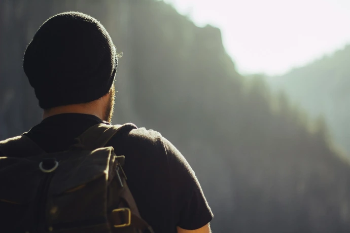 man wearing black t-shirt and knit cap fronting mountains